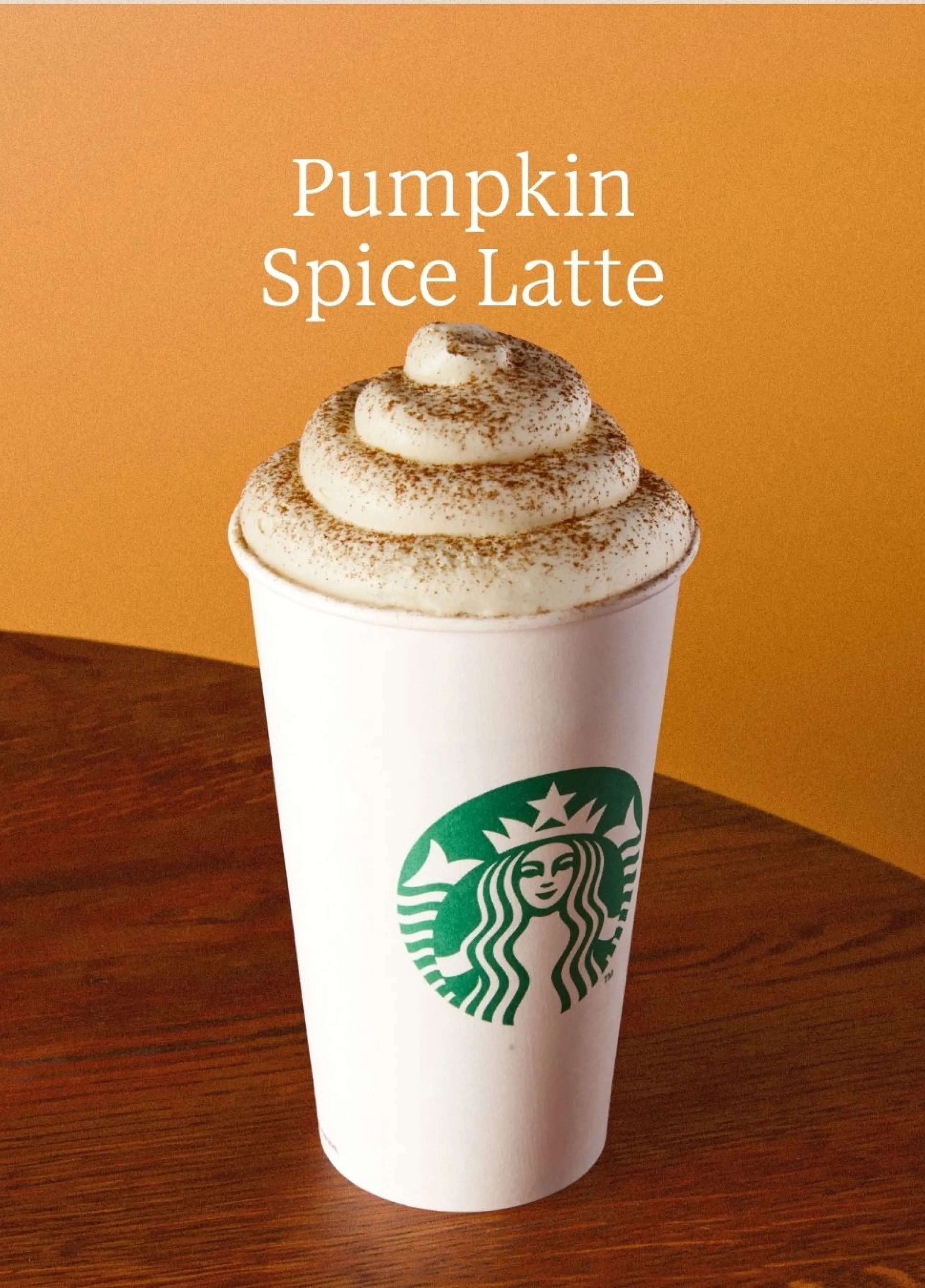 Kubek Starbucks z Pumpkin Spiced Latte, udekorowany bitą śmietaną i przyprawami, na pomarańczowym tle z napisem „Pumpkin Spice Latte”.