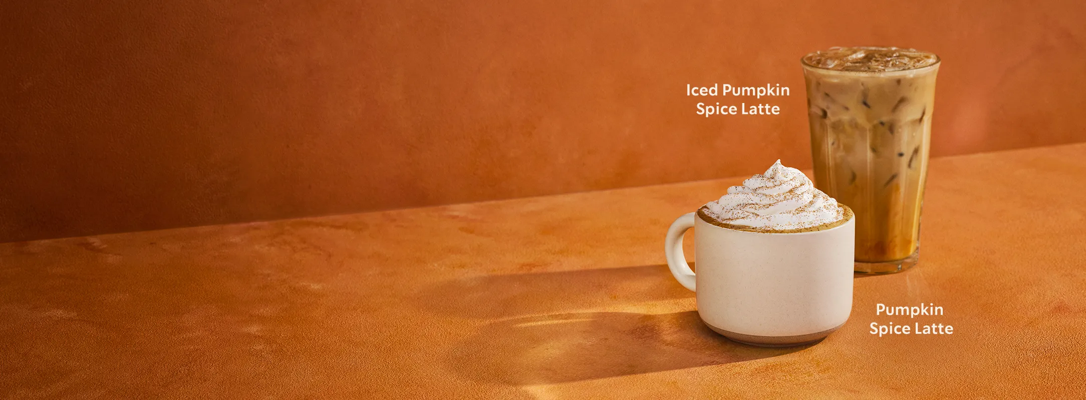 Gorąca i mrożona Pumpkin Spice Latte na pomarańczowym tle.